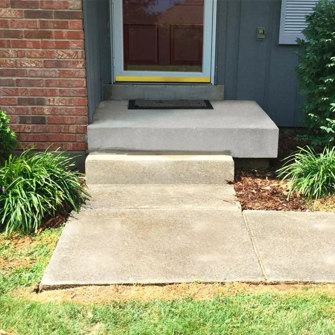 Front entryway concrete porch landing lifted flush with the door threshold and brick wall.