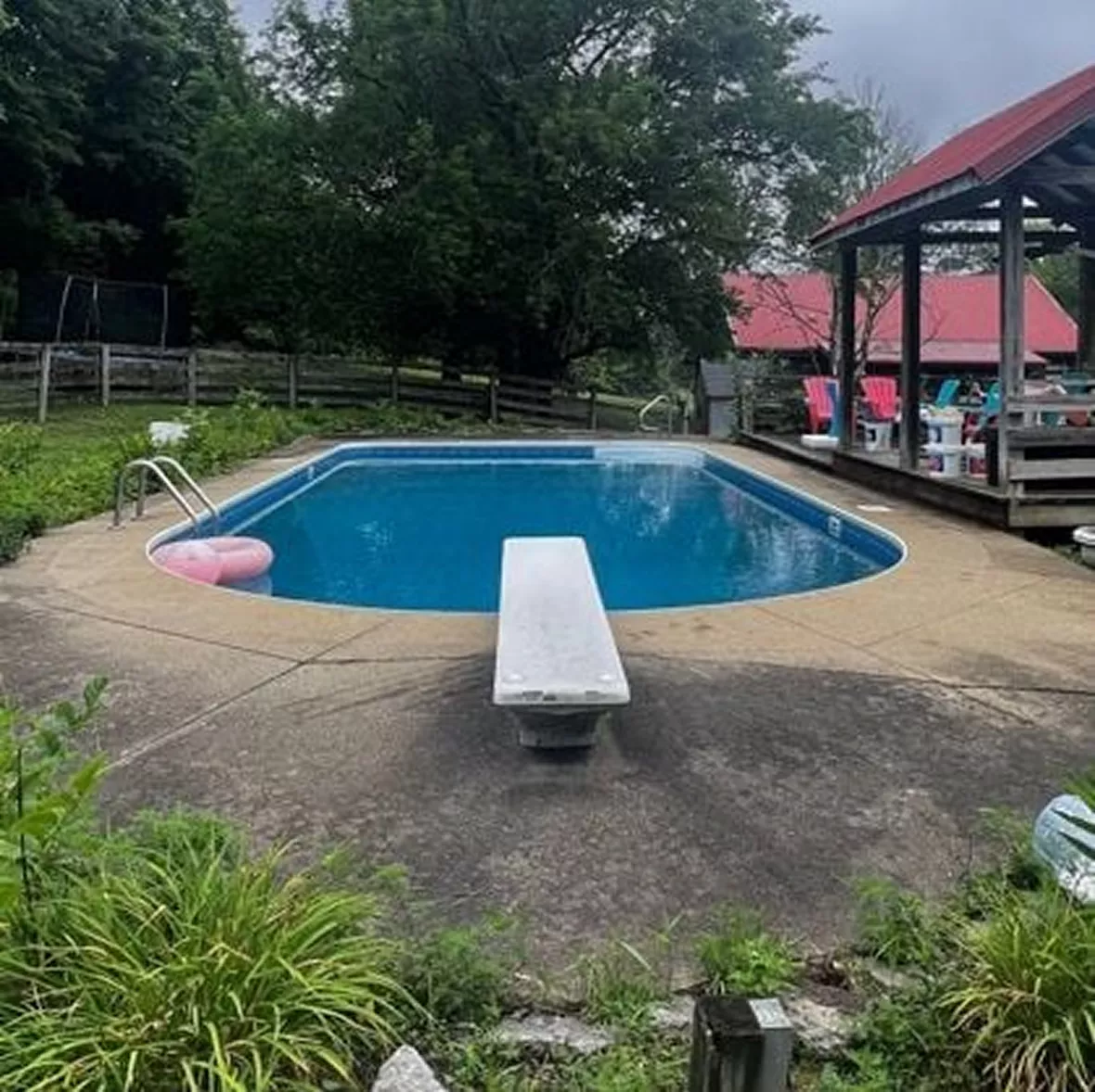 Settled Concrete Pool Deck – Before Poly Concrete Repair Weathered, sunken concrete pool deck with uneven slope near the diving board and fence line.