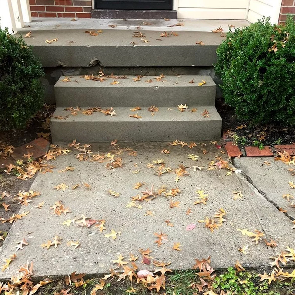 Tilted Concrete Entry Steps – Before Poly Foam Leveling Uneven concrete porch steps sinking on one side between landscaping bushes.